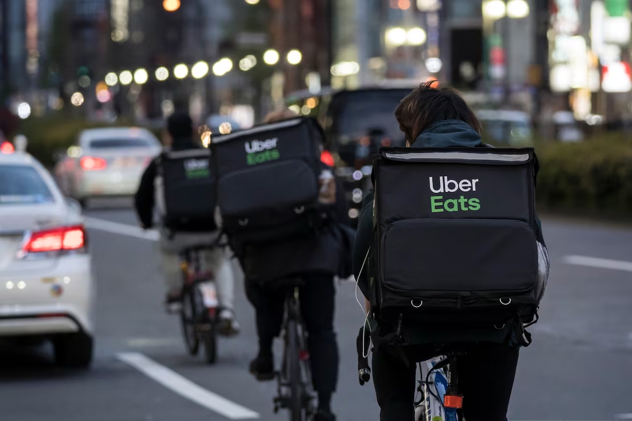 Three Uber Eats couriers are visible, riding down the street delivering orders on bicycles.